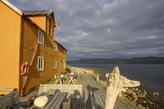 Wooden building on fjord shore under heavily cloudy sky, Veidnes, Kongsfjord, Finnmark, Norway