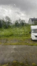 Looking through the rainy glass of a window, rain dripping along the window, cloudy sky, motorhome