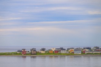 View of the port city of Vardø with a row of small colorful houses under blue sky with some clouds,