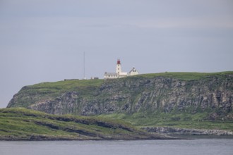 White lighthouse with red tip and antennas rises above steep rocks on the bird island of Hornoya,