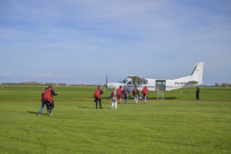People with parachute equipment in front of a small plane on a green field, taking off for a tandem