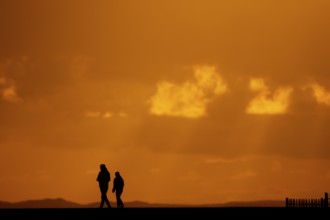 Two people walking in silhouette in front of an orange sunset on the horizon, Texel Island, Den