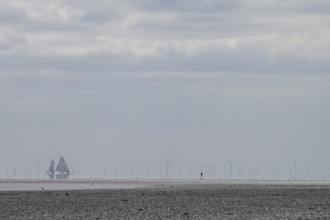 Lonely mudflats scene with wind turbines and sailing ships in the distance, grey landscape with