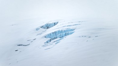Smooth white snowy area on the glacier broken by crevasses with blue rugged glacial ice, detail,
