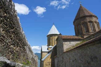 Historic monastery complex with brick towers and a surrounding stone wall under a blue sky, Ananuri