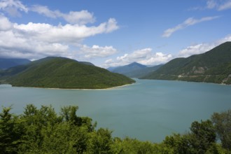 Idyllic landscape with a large lake surrounded by green mountains under a blue sky with clouds,