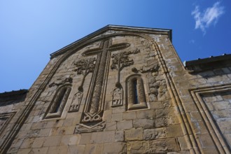 Historic church façade with large cross reliefs and decorations under a blue sky, Ananuri Castle,
