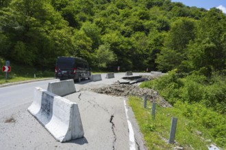 A black van drives on a damaged mountain road with concrete barriers, camper drives on road near