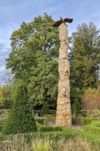 Tree trunk with carvings like a totem pole, stylized eagle on top in front of Schellenberg hunting