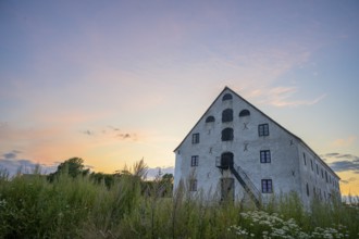 A historic stone building under a colorful evening sky at sunset, old merchant magazine, Südpunkt