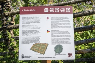 Information sign about Kålgården with texts in various languages and symbols, a picturesque garden