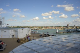 View from the ship deck of a TT-Line ferry with people and city in the background under a blue sky,