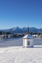 A small chapel against snow-covered mountains and clear blue sky in a winter landscape,