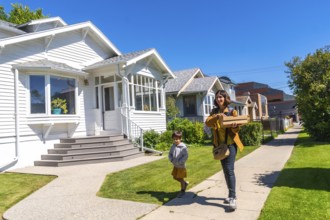 Mother and son carrying packages walking on a sidewalk in a residential neighborhood in calgary,