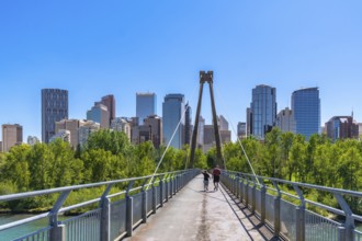 Two tourists are jogging across a pedestrian bridge in calgary, alberta with the downtown skyline