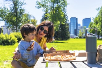 Mother and son are sharing a pizza picnic lunch together on a sunny day at a park in calgary,