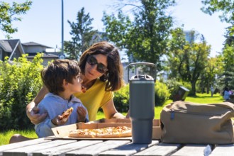 Mother and her son are enjoying a pizza picnic together on a sunny day in a calgary park, creating