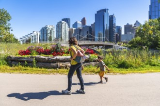 Mother with backpack walking with her running son in calgary's east village riverwalk, enjoying a