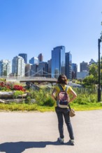 Tourist with a backpack stands in a colorful park, gazing at the modern cityscape of calgary,