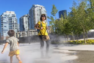 Tourist in a yellow shirt and backpack smiling while child runs through a refreshing misting system