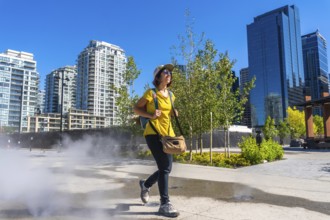 Female tourist walking through a refreshing misting station in calgary's east village, enjoying a