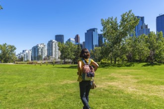 Female tourist with backpack walking on green grass in a park, enjoying the view of modern