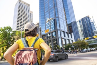 Young female tourist with backpack admiring modern skyscrapers in calgary's downtown district, a