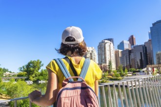Young woman with backpack standing on peace bridge, admiring modern architecture and cityscape of