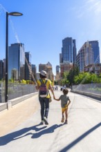 Mother and son enjoying a sunny day walking on a bridge in calgary city center, with skyscrapers