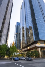 Glass skyscrapers reflecting surrounding buildings rise high above a street with cars passing by in