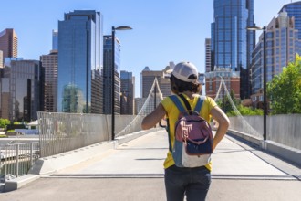 Young tourist with backpack walking on bridge exploring calgary cityscape on sunny summer day,