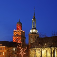 The Christmassy illuminated town hall tower and the illuminated church tower of St. John's Church