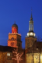 The Christmassy illuminated town hall tower and the illuminated church tower of St. John's Church