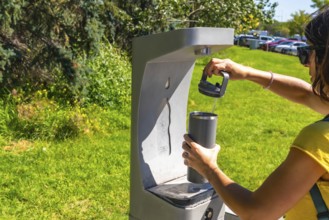 On a sunny day, a tourist is filling her reusable water bottle at a public drinking water fountain