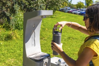 Tourist filling her reusable, eco friendly water bottle at a public drinking water fountain in a