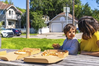 Happy child enjoys a slice of pizza with his mother at a picnic table in a residential neighborhood