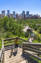 Tourists enjoying a sunny day walking down wooden stairs in a park overlooking the calgary skyline,