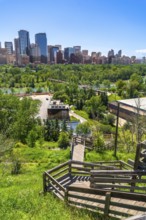 Wooden staircase winding down a grassy slope, leading towards the modern cityscape of calgary,