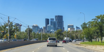 Vehicles are driving on a highway with the calgary skyline, featuring modern skyscrapers and lush