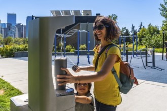 Tourist is filling reusable water bottle at a modern public drinking water fountain with calgary