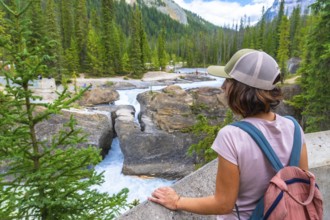 Female tourist wearing a baseball cap and backpack, admiring the bow river natural bridge in banff