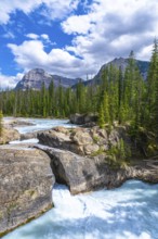 Turquoise water flows under natural bridge rock formation on bow river with evergreen trees,