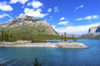 Turquoise water reflecting imposing mountains and a rocky islet with coniferous trees under a