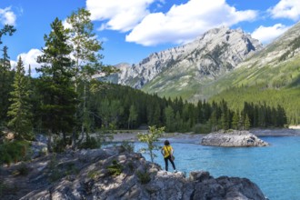 Tourist standing on rocks by the turquoise waters of lake minnewanka, admiring the breathtaking