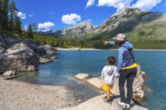 Mother points across the turquoise expanse of lake minnewanka, sharing a moment of awe with her son