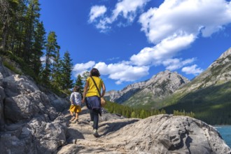 Mother and child hiking on a rocky trail, enjoying the scenic view of lake minnewanka and the