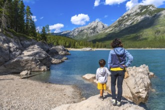 Mother and son standing on a rock, admiring the stunning turquoise waters of lake minnewanka,