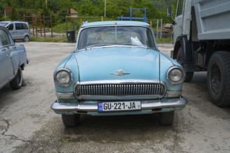 A blue classic car is parked in a parking lot next to a truck, GAZ M-21 Volga, Georgia