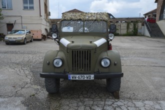 A green vintage car is parked in front of a building, Soviet all-wheel drive off-road vehicle,