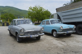 Two vintage cars are parked in a parking lot in front of a hilly landscape, GAZ M-21 Volga, Georgia